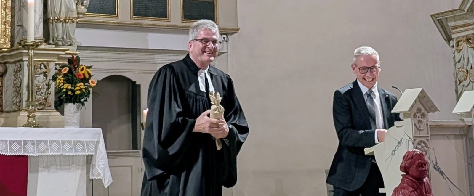 Zwei männlich gelesene Personen in Talaren in einer Kirche.