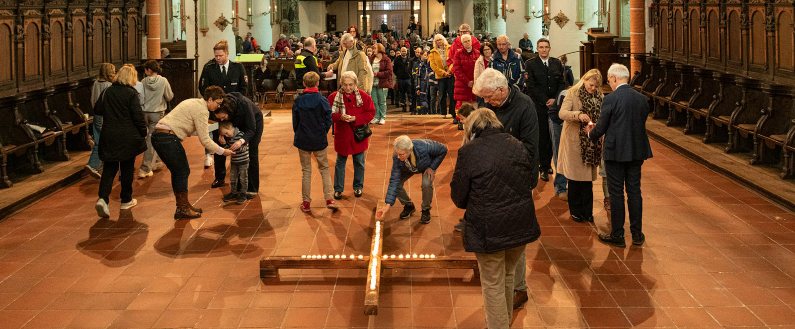Blick in eine Kirche, in der Menschen mit Kerzen ein Kreuz legen.