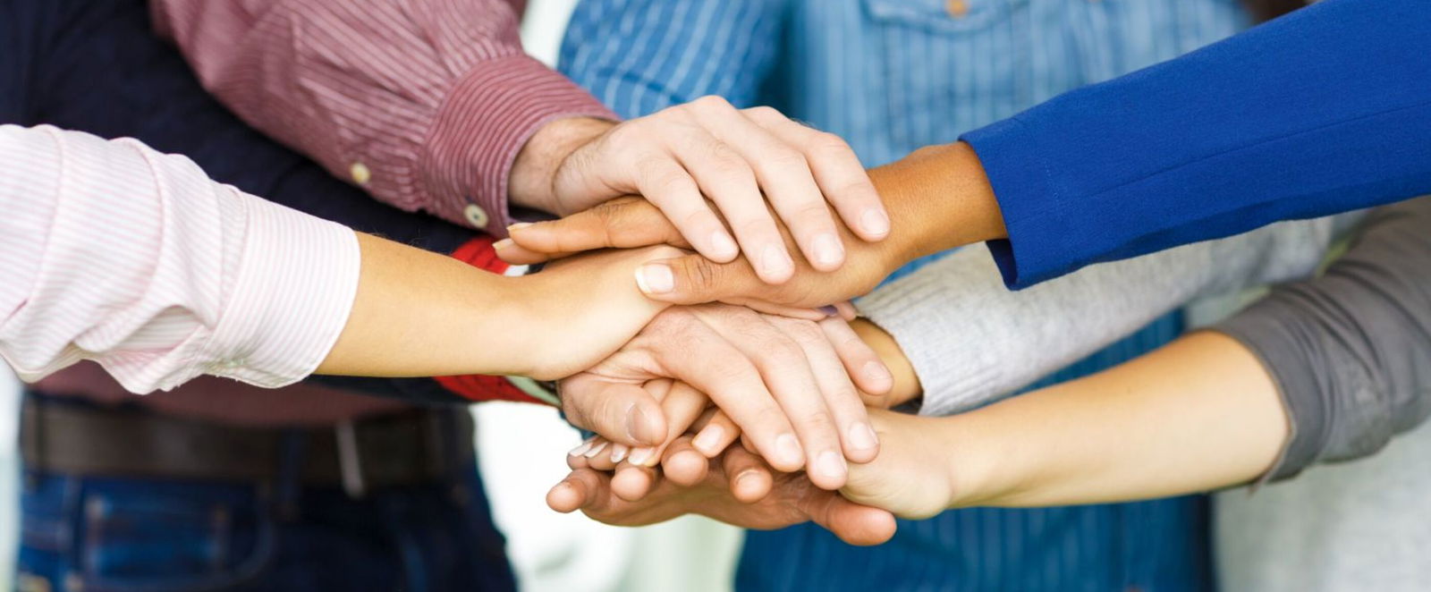 Mehrere Menschen unterschiedlicher Hautfarben legen ihre Hände übereinander.