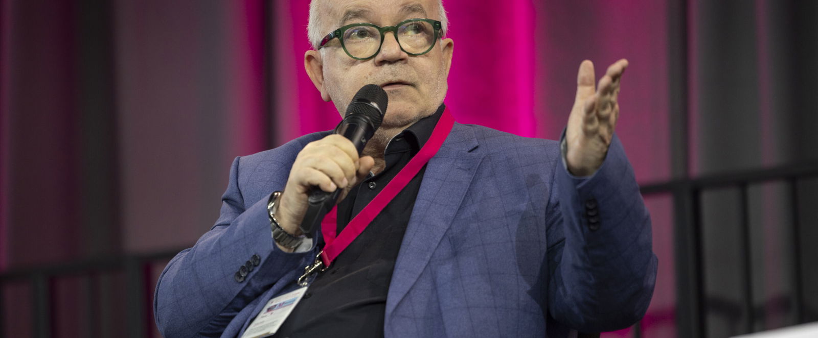 Eine als Mann gelesene Person mit Brille und hoher Stirn spricht in ein Mikrofon.