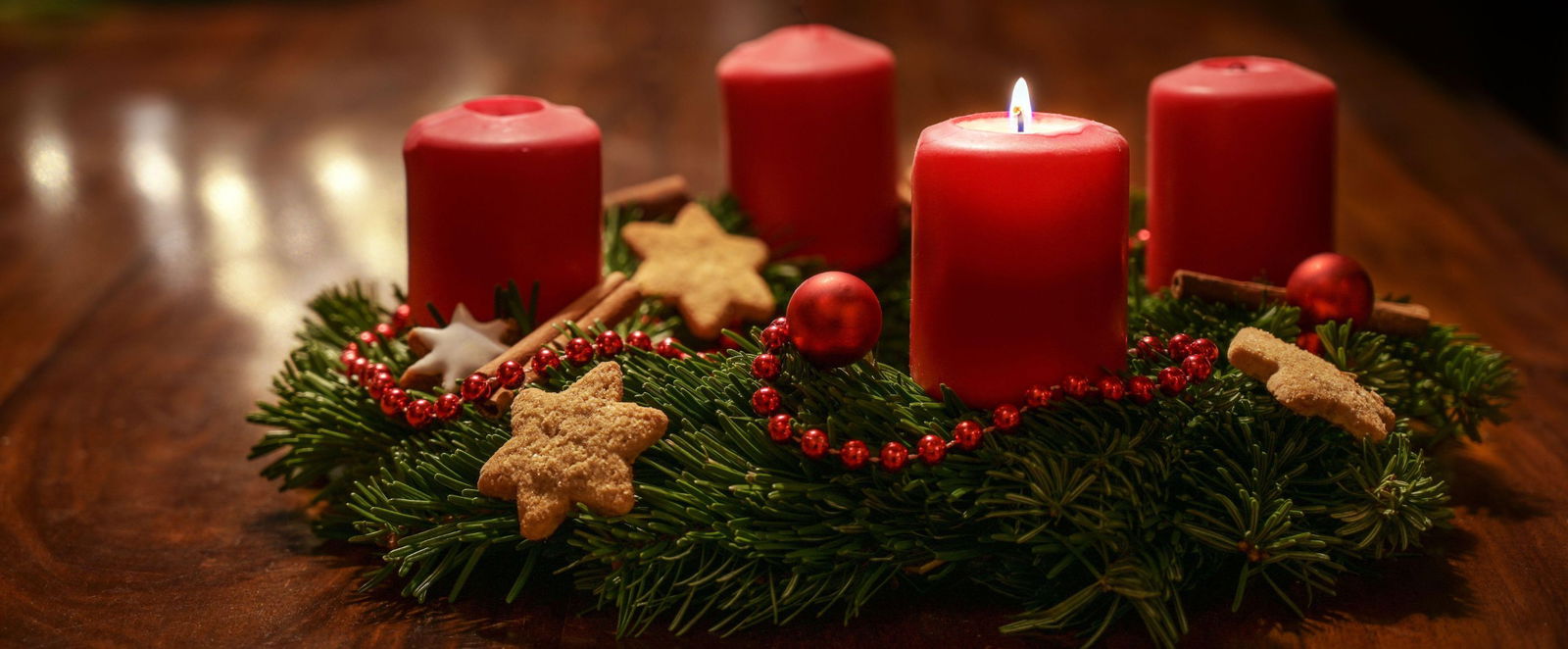 Ein Adventskranz mit roten Kerzen, bei dem eine Kerze brennt.