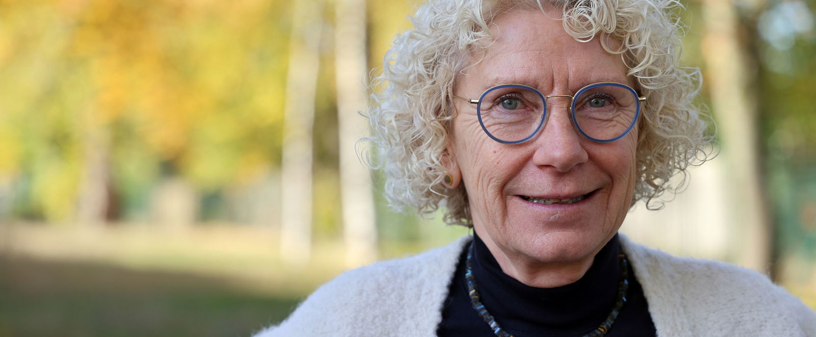 Eine als Frau lesbare Person mit grauen Locken und Brille.