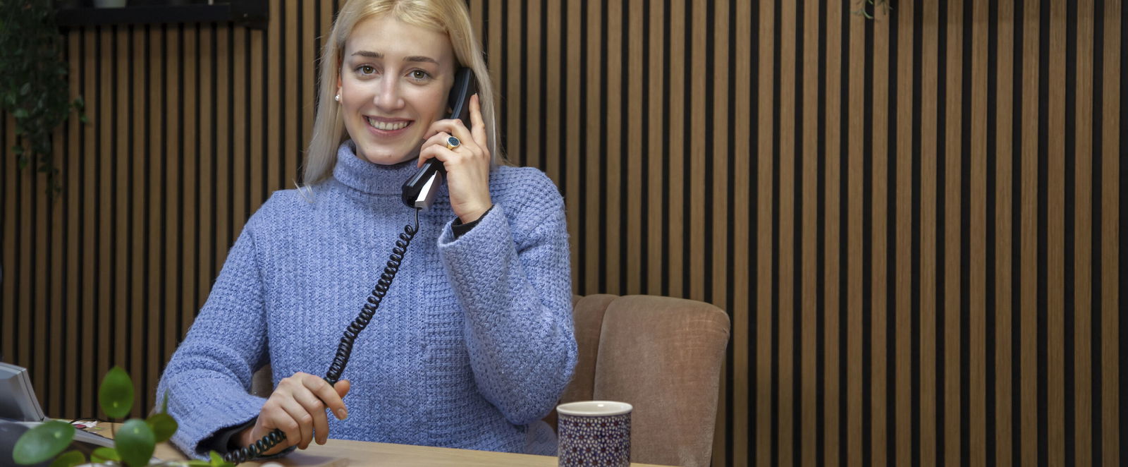 Eine als Frau lesbare Person sitzt an einem Tisch und telefoniert.