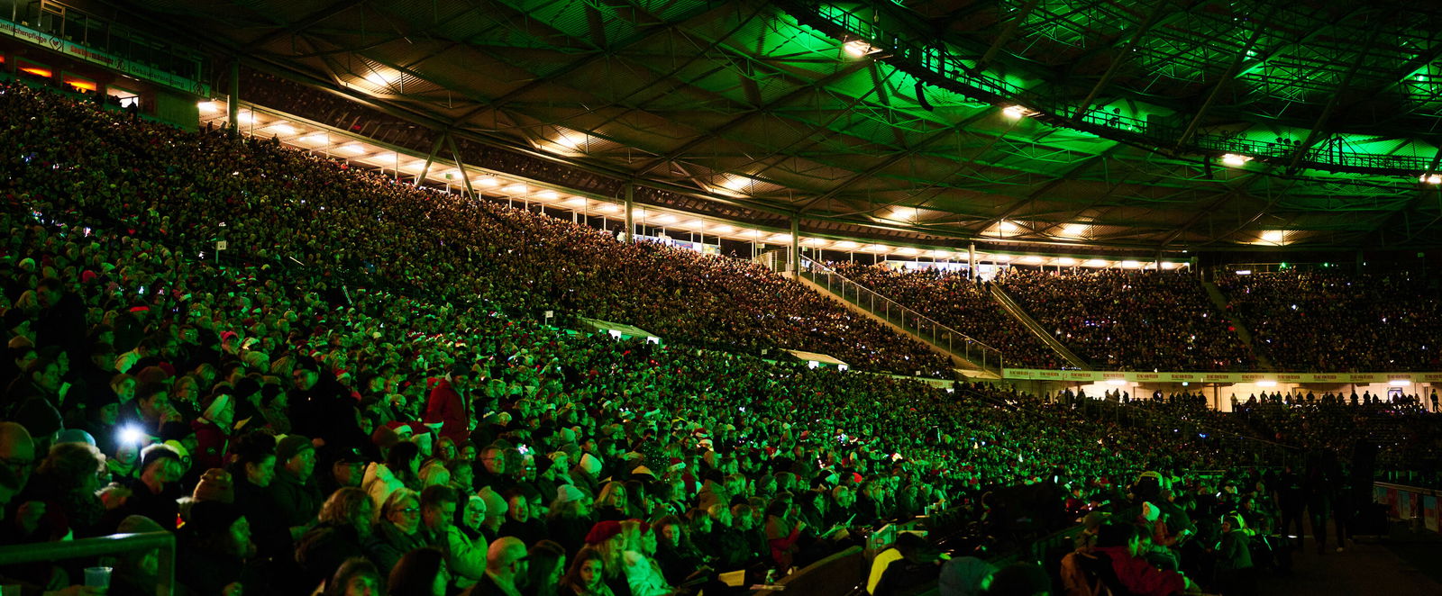 Viele tausend Menschen in einem grün erleuchteten Stadion.