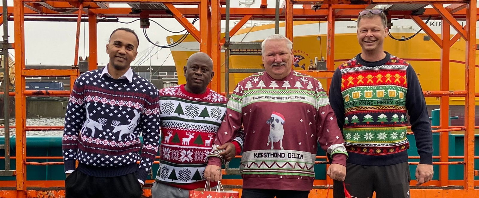 Vier Männer tragen Weihnachtspullover und Geschenktüten.