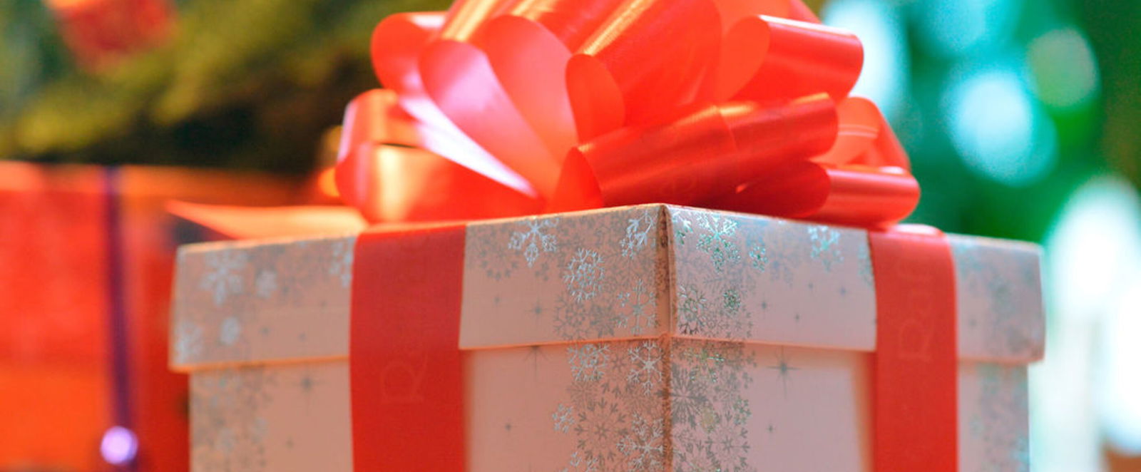 Ein weiß-silberner Karton mit roter Schleife vor einem Weihnachtsbaum.