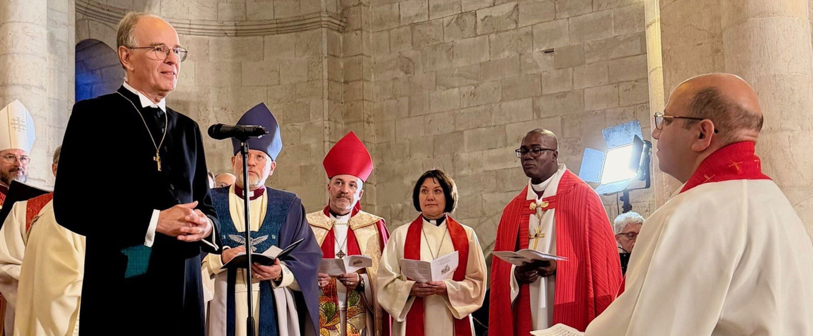 Mehrere als Männer lesbare Personen in Bischofskleidung stehen zusammen.