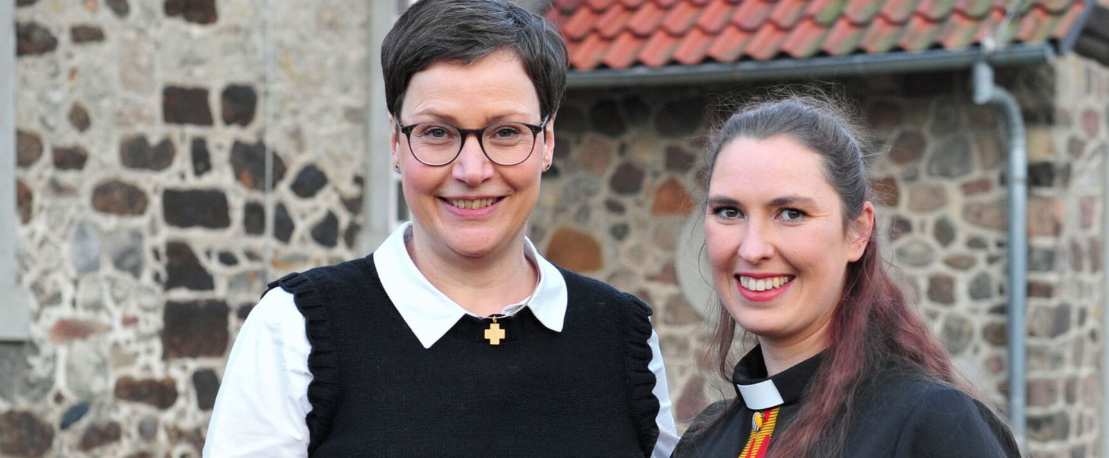 Zwei als Frauen lesbare Personen vor einer Kirche.