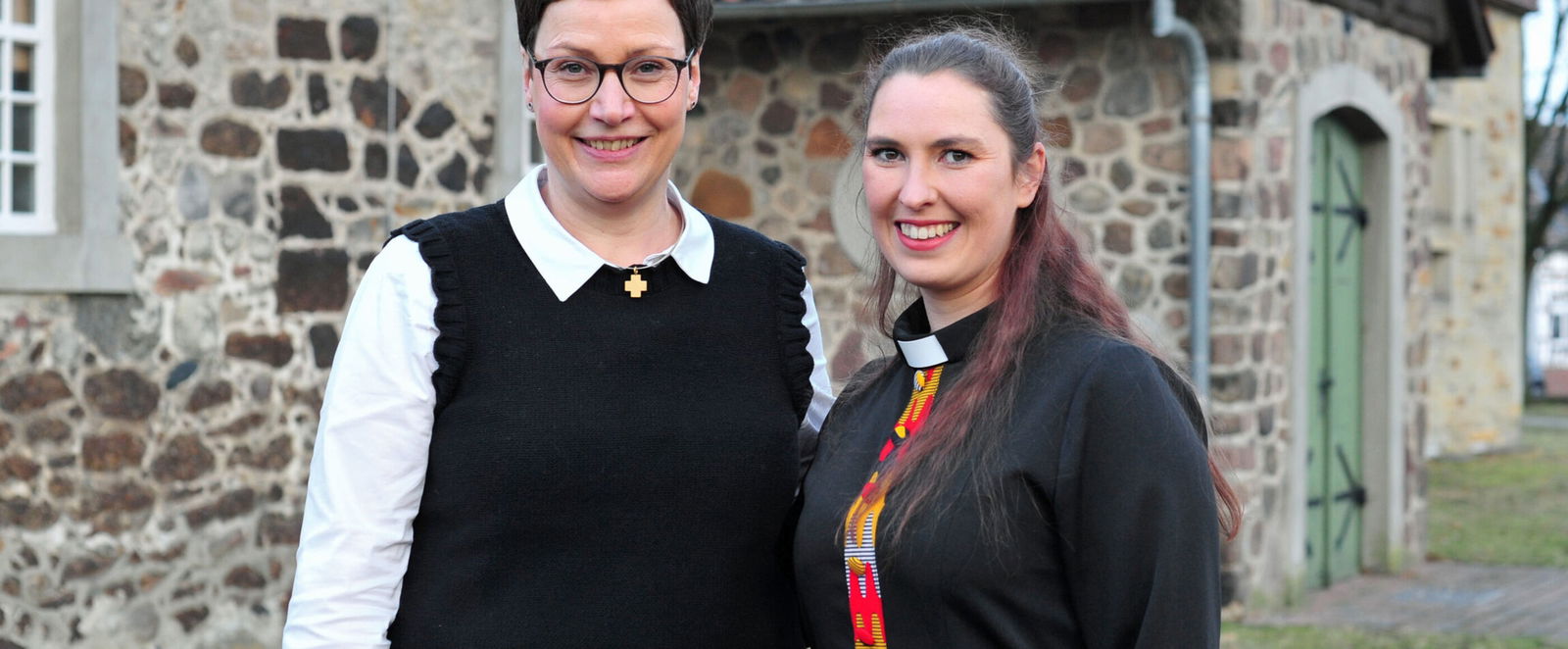 Zwei als Frauen lesbare Personen vor einer Kirche.