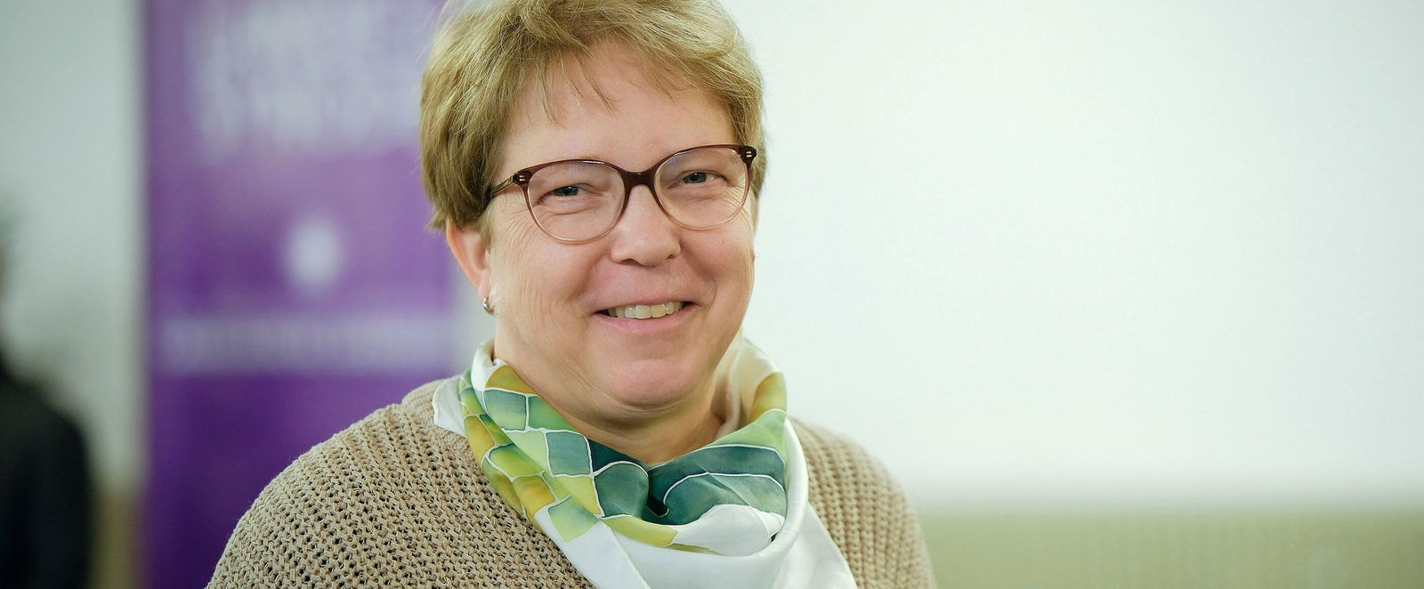 Eine weiblich gelesene Person mit kurzen, blonden Haaren und Brille.