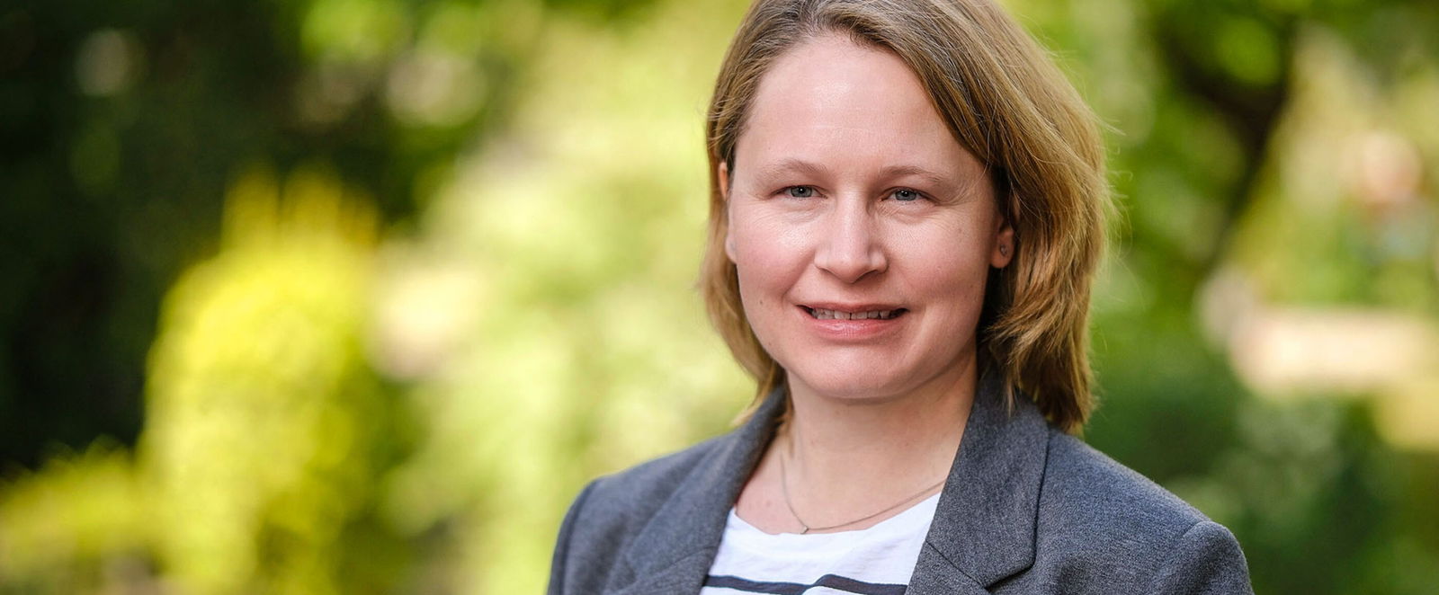 Portraitfoto einer als Frau lesbaren Person vor einem grünen Hintergrund