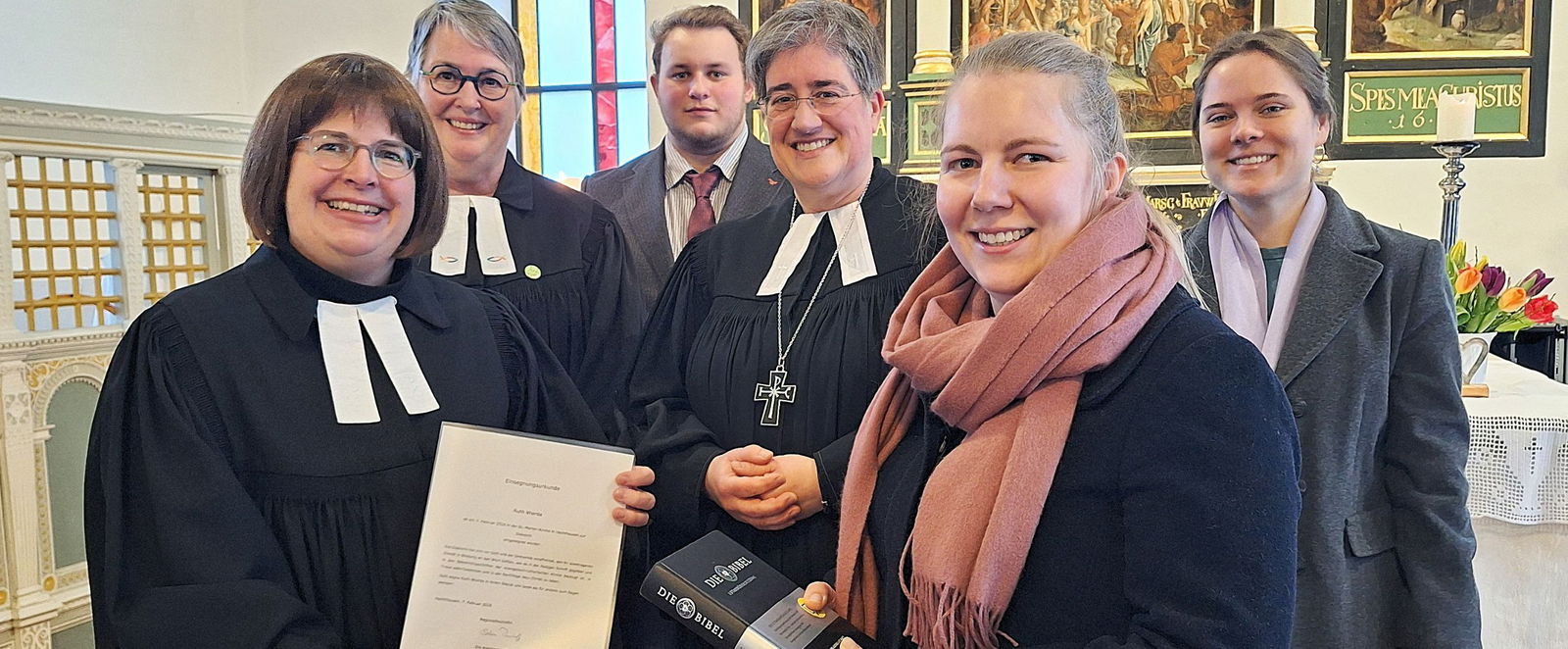 Menschen stehen mit einer Urkunde und Bibel und zum Teil im Talar in einer Kirche.