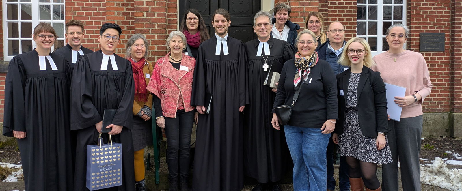 Eine Gruppe Menschen vor einer Kirche, einige tragen einen Talar.
