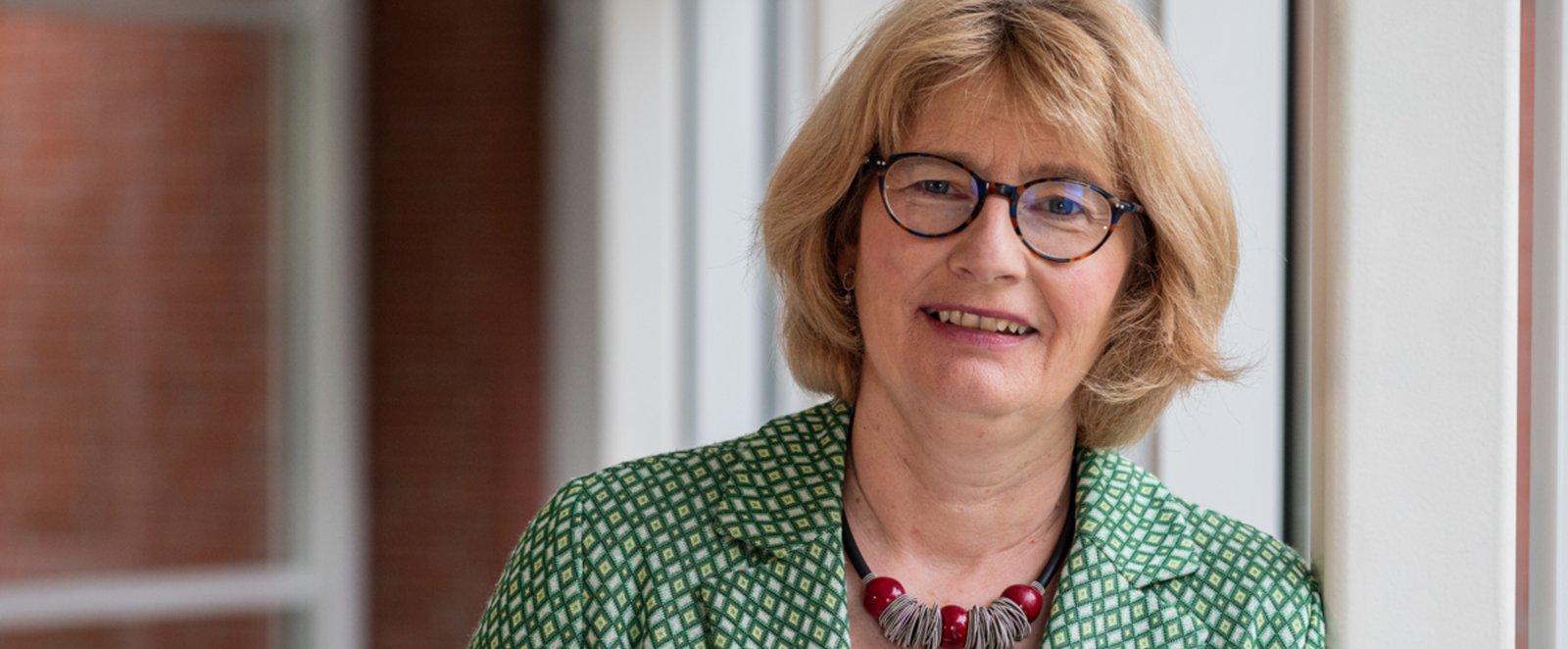 Eine weiblich gelesene Person mit blonden Haaren, grünem Jackett und Brille.