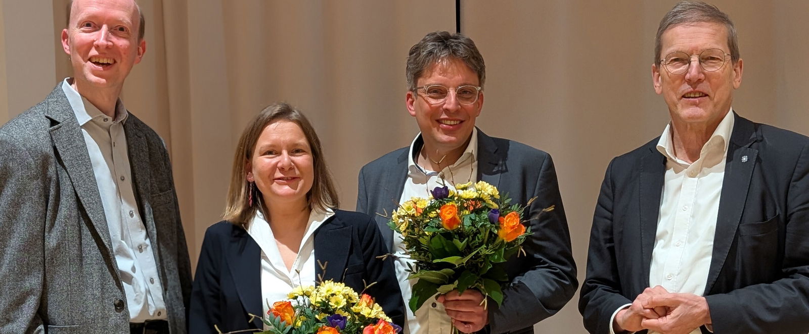 Vier Menschen stehen für ein Gruppenfoto zusammen, zwei davon mit Blumenstrauß.