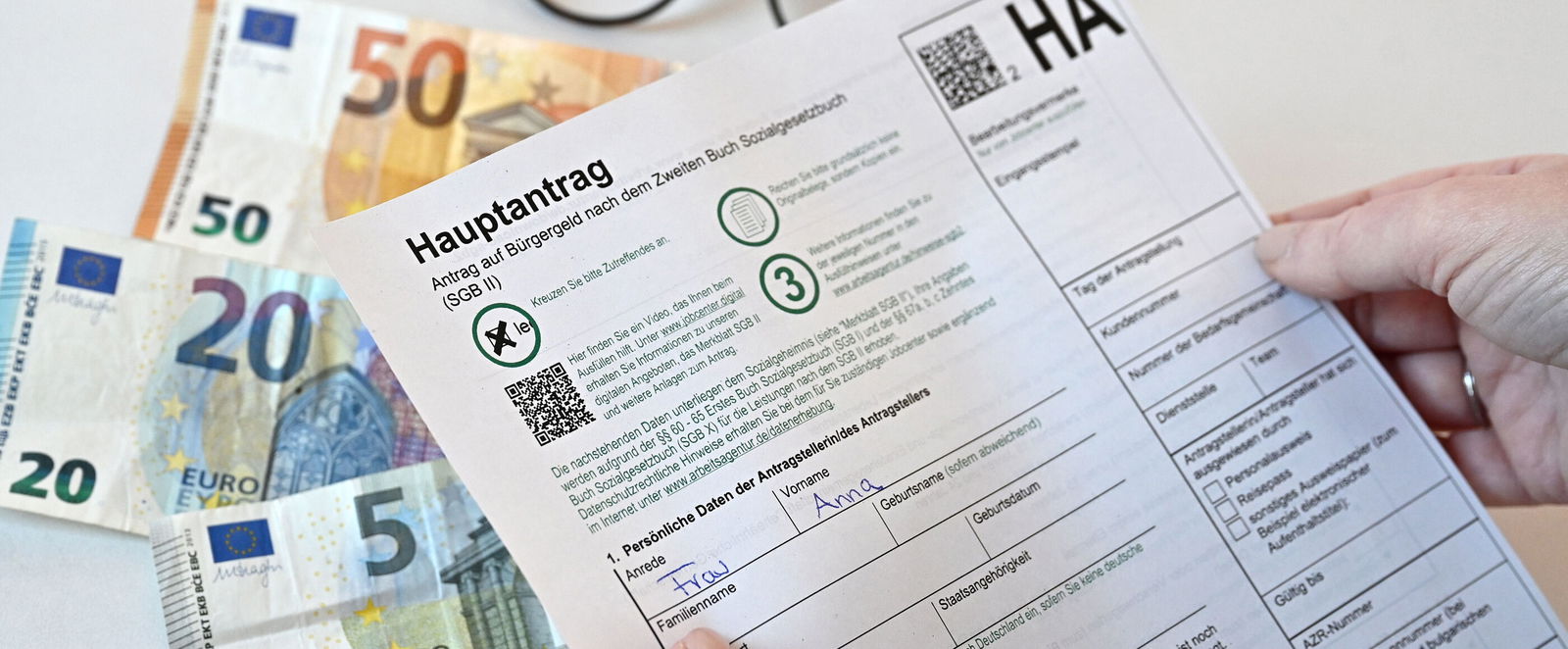 Ein Antrag auf Bürgergeld, im Hintergrund liegen Geldscheine