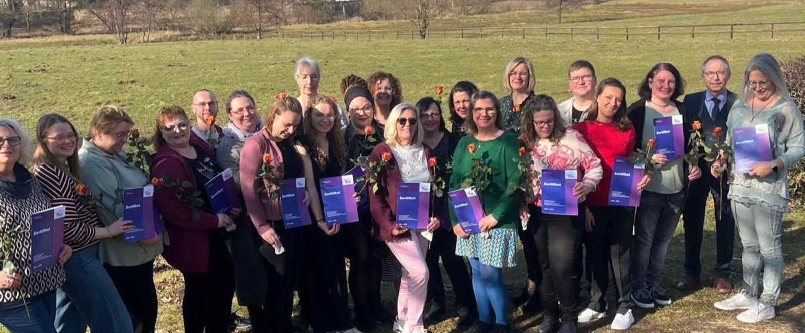 Etwa zwei Dutzend Menschen stehen auf einem Feld unter blauem Himmel.