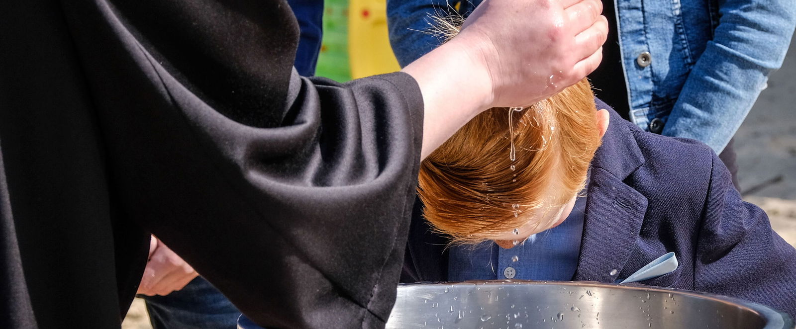 Eine Hand träufelt einem Täufling Wasser über den Kopf