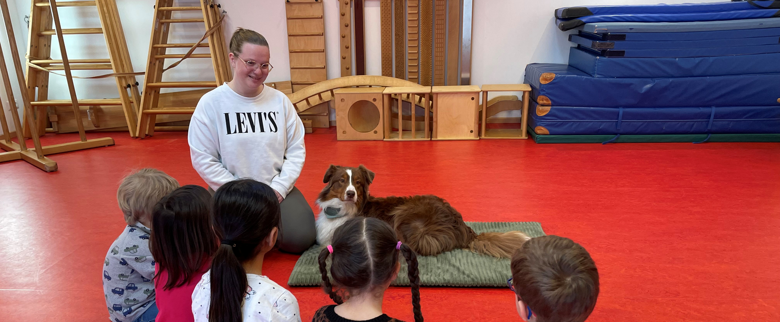 Ein Hund liegt auf einer Matte neben Kindern und einer erwachsenen Person.