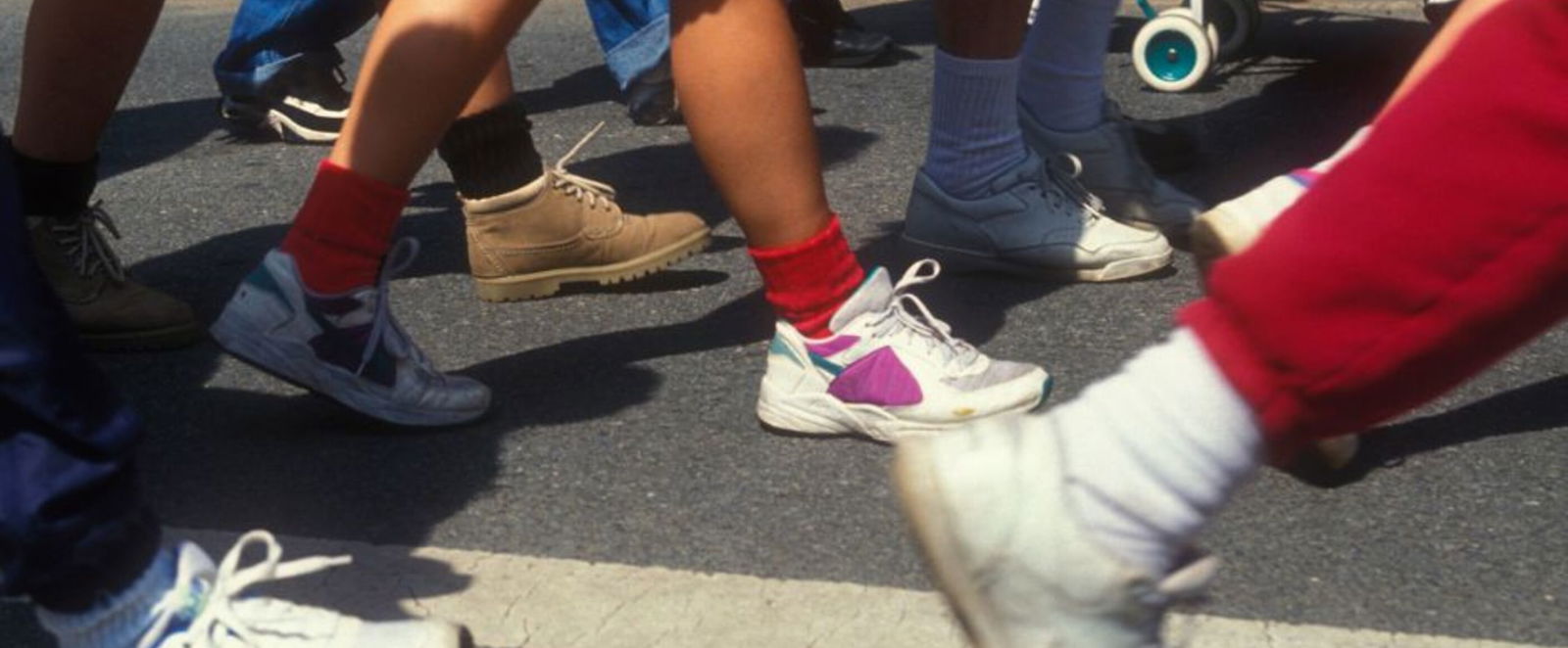 Nahaufnahme mehrerer Beinpaare, die eine Straße entlanglaufen.