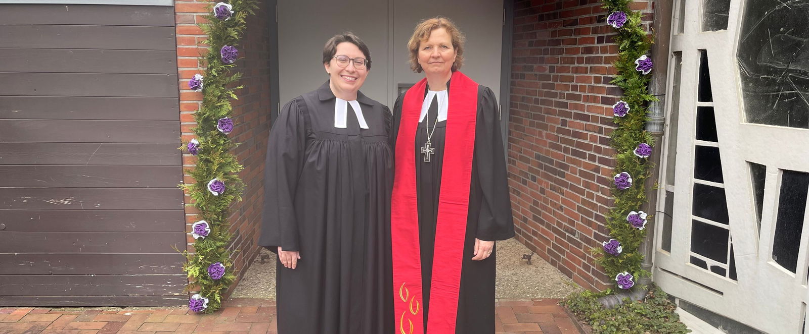 Zwei Frauen im Talar vor einem Blumenbogen