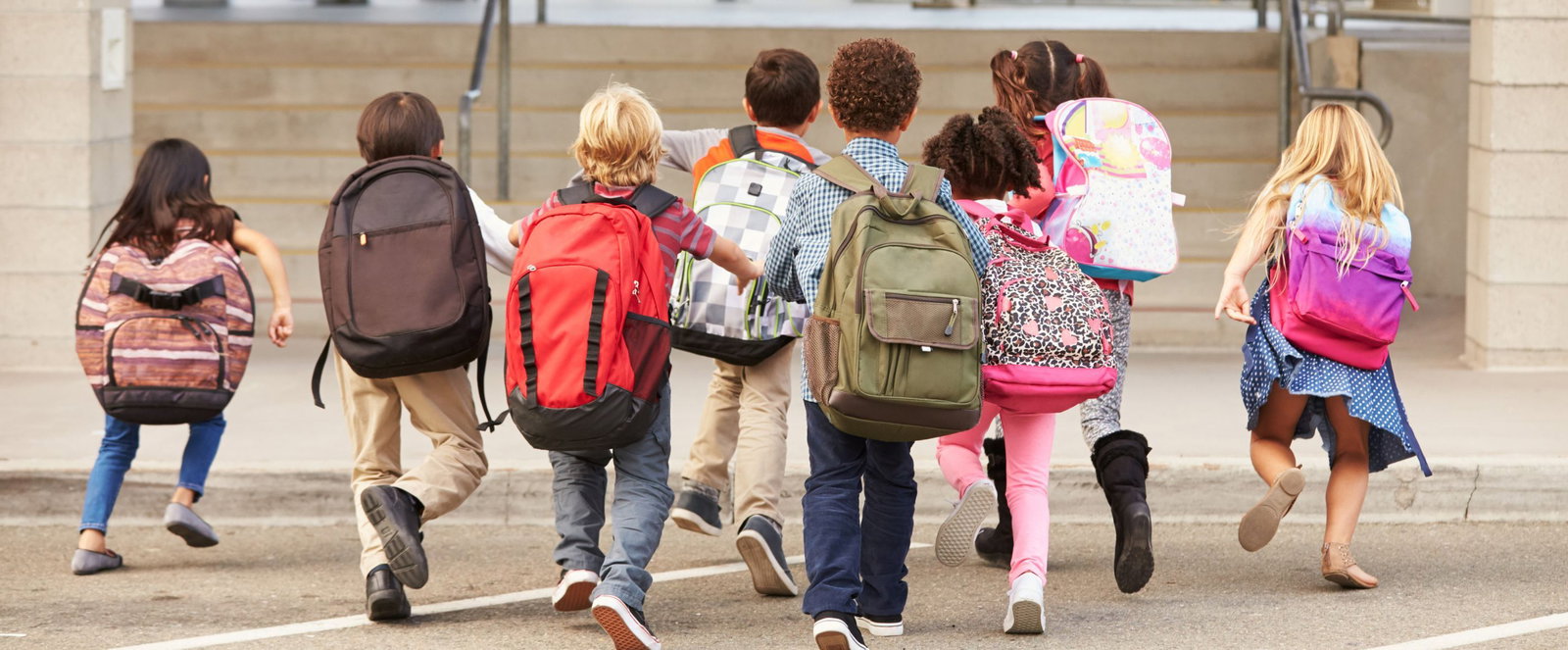 Kinder mit Schulranzen rennen auf dem Schulhof umher.