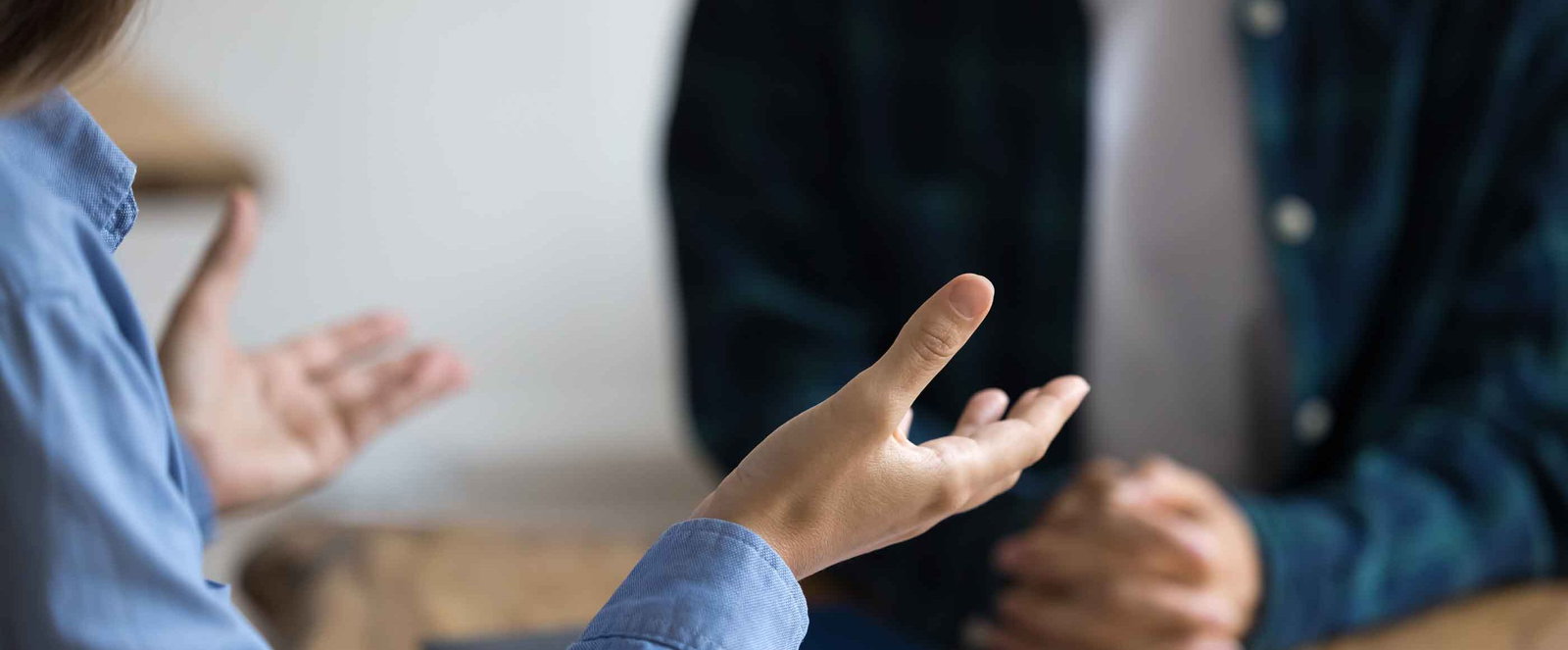 Zwei Personen sitzen an einem Tisch und reden. Eine gestikuliert. Die Köpfe sind nicht zu sehen.