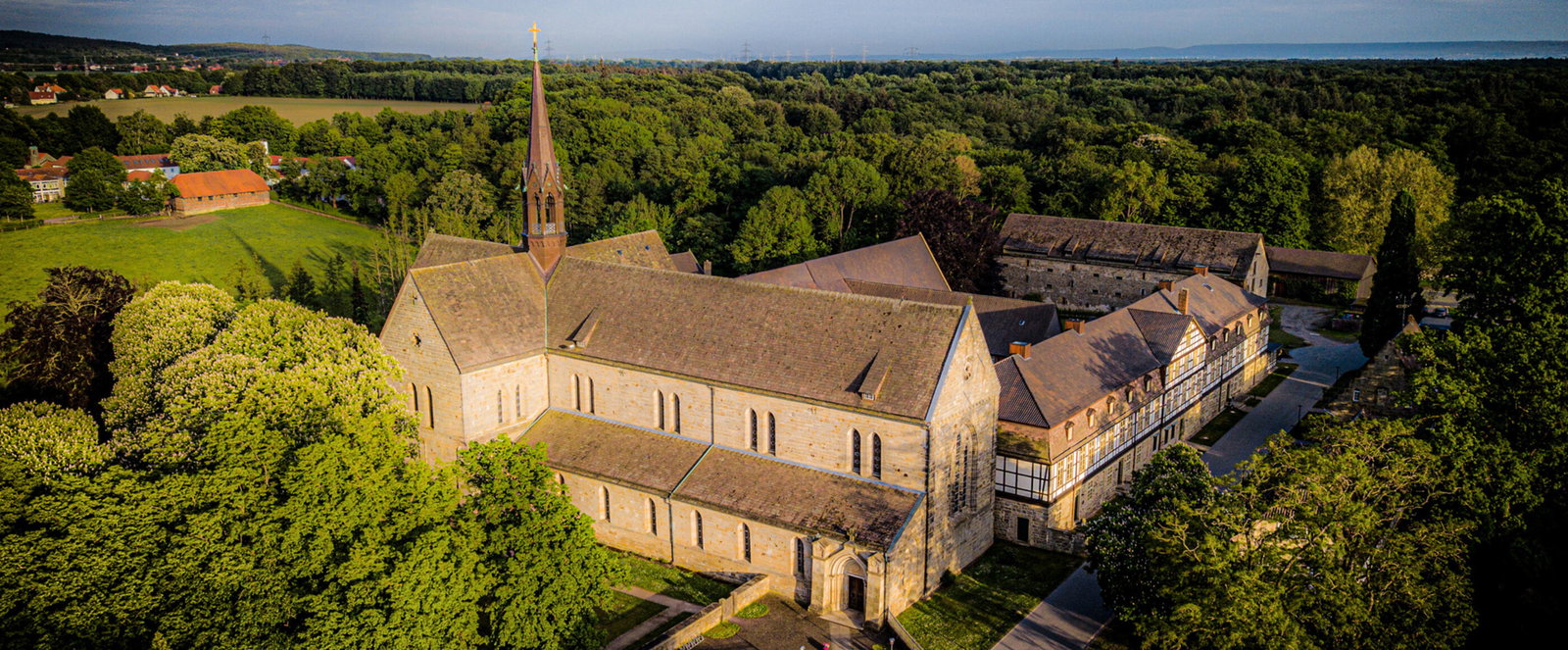 Eine große historische Kirche mit angrenzenden Fachwerkgebäuden inmitten mehrerer Bäume.