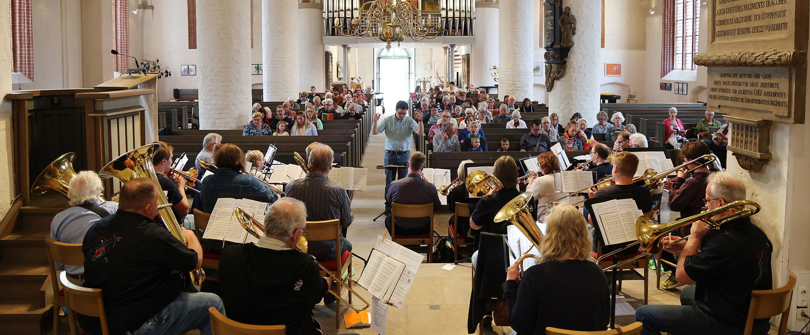 Viele Menschen singen gemeinsam mit einem Posaunenchor in einer Kirche.