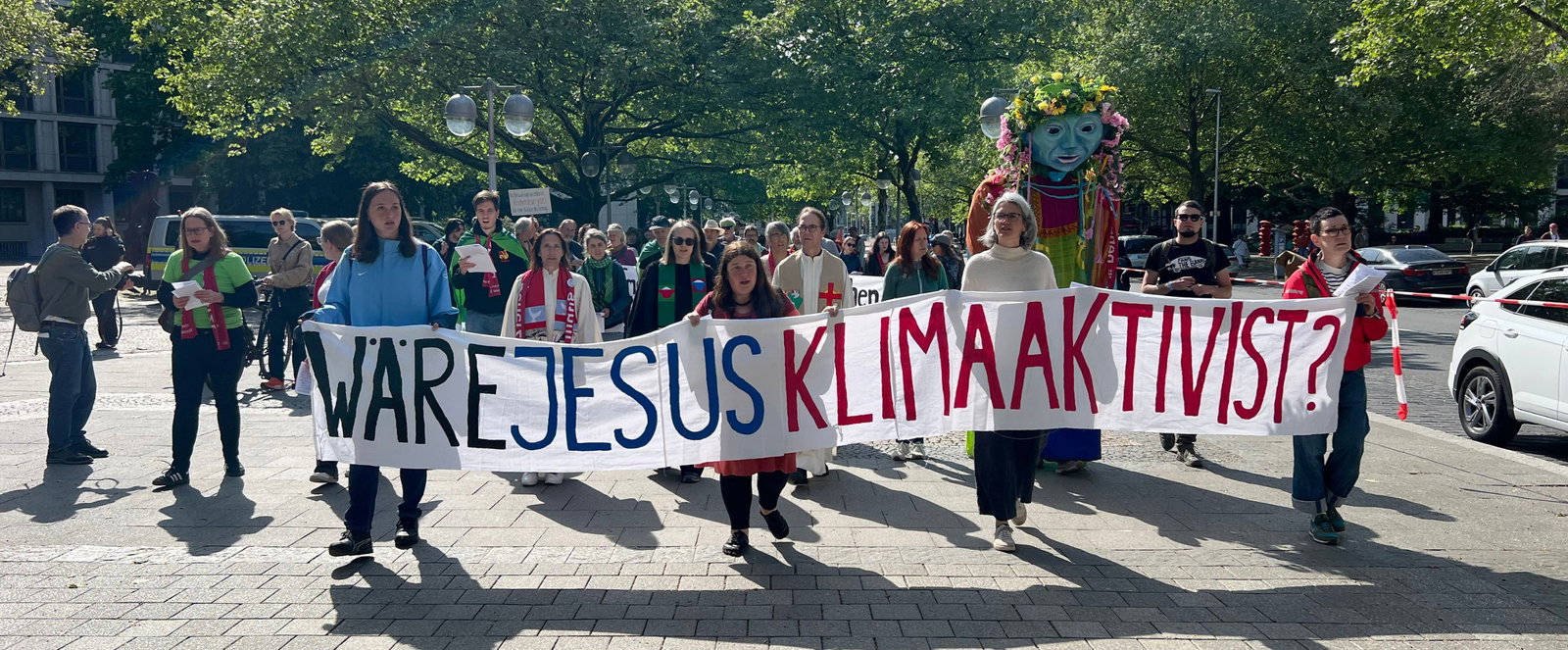 Menschen auf einer Demonstration, sie halten ein Banner, auf dem steht "Wäre Jesus Klimaaktivist?".