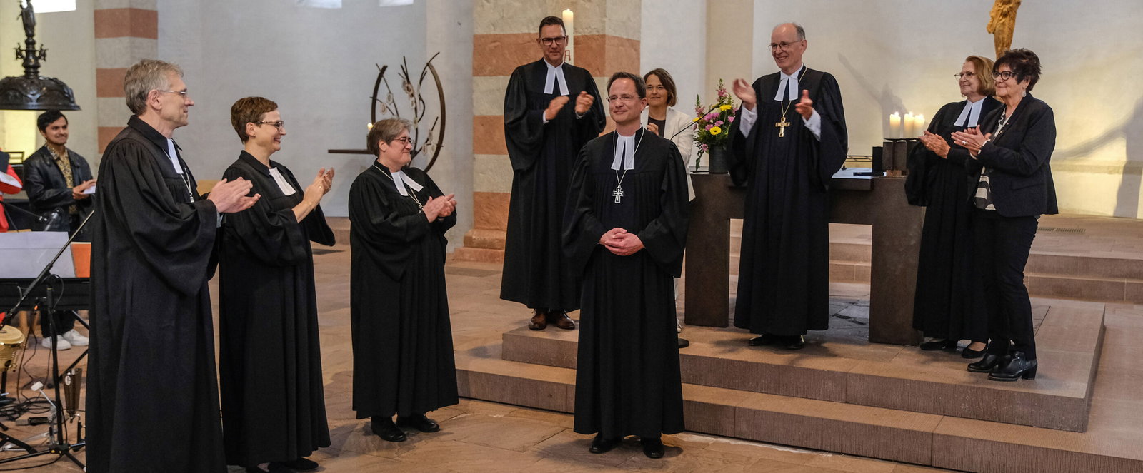 Mehrere als Männer und Frauen lesbare Personen stehen in einem Altarraum und applaudieren.