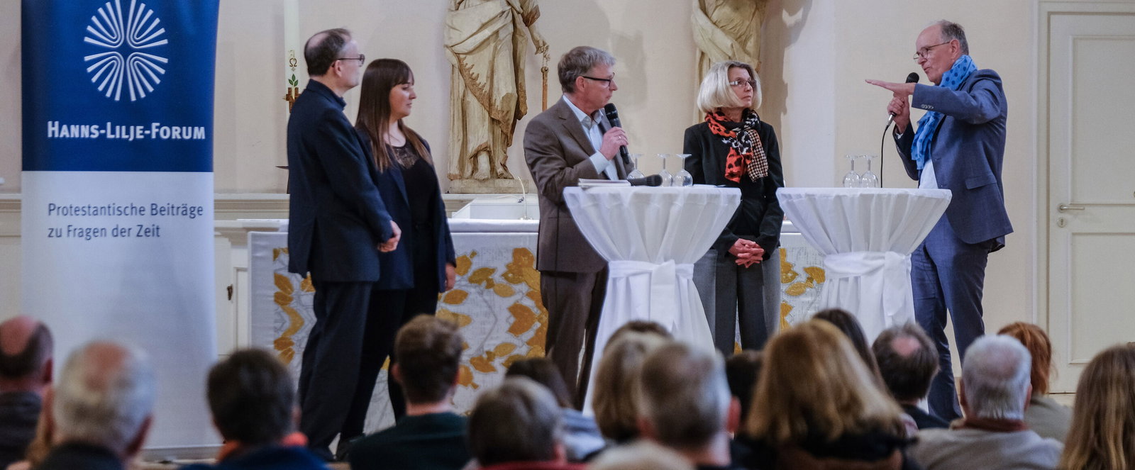 Eine Gruppe steht an Stehtischen und diskutiert.
