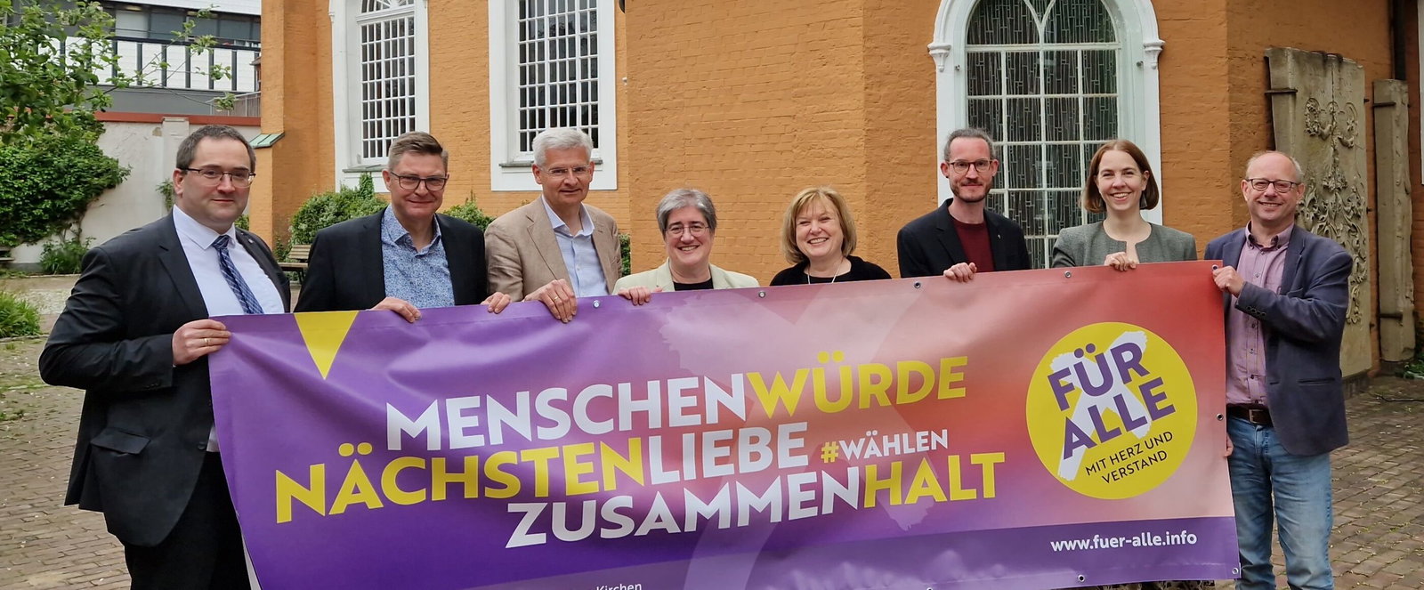 Mehrere als Frauen und Männer lesbare Personen halten ein Banner mit den Worten Menschenwürde, Nächstenliebe, Zusammenhalt