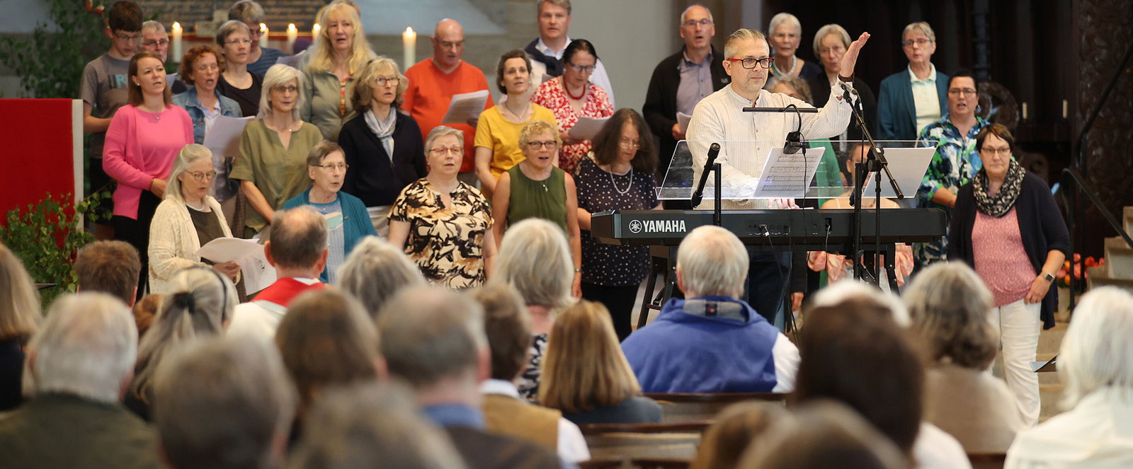 Ein Chor und eine Kirchengemeinde singen gemeinsam, ein Chorleiter dirigiert.