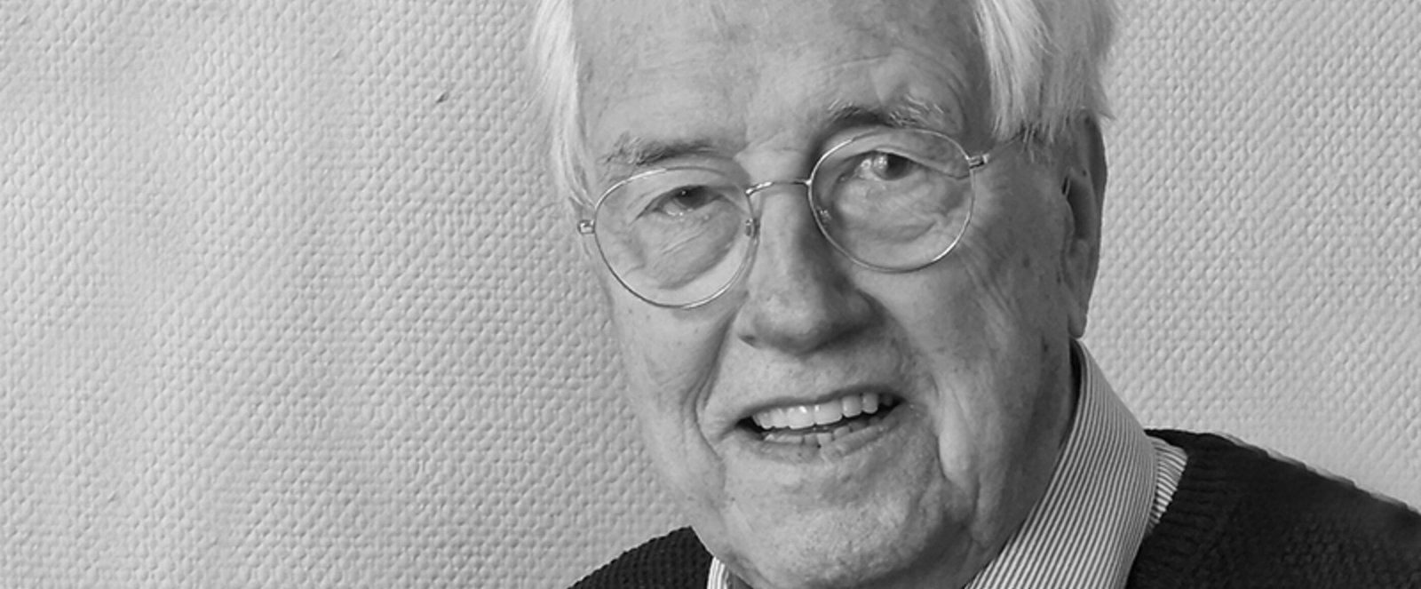 Schwarzweiß-Portrait von einer als Mann lesbaren Person mit Brille und grauem Haar.
