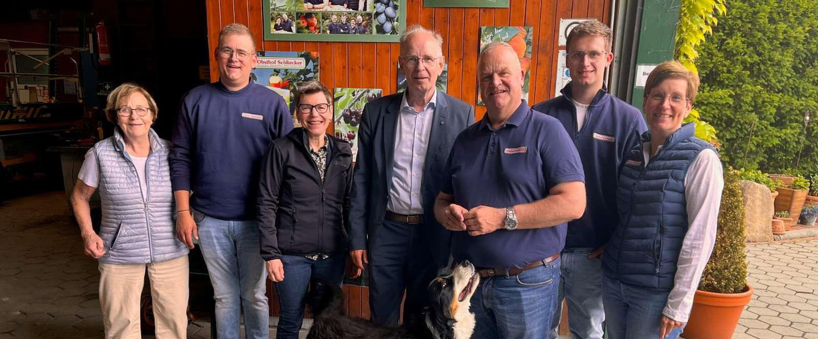 Mehrere als Männer und Frauen lesbare Personen und ein Hund auf einem Hof.