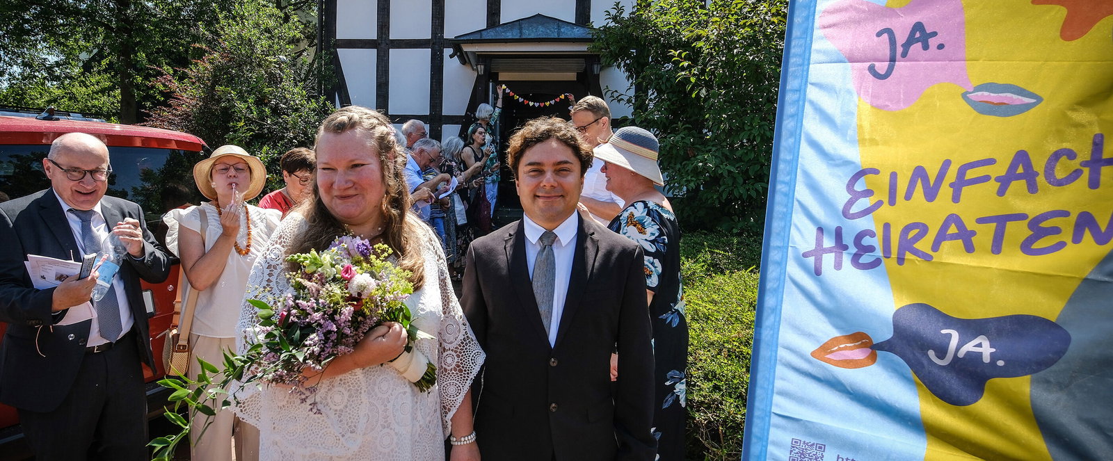 Eine Hochzeitsgesellschaft begrüßt ein Paar, das aus der Kirche kommt.