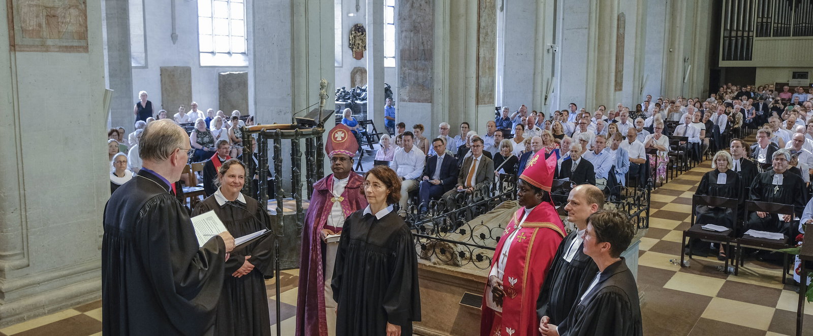 Mehrere Menschen im geistlichen Gewand stehen im Altarraum einer vollbesetzten Kirche.