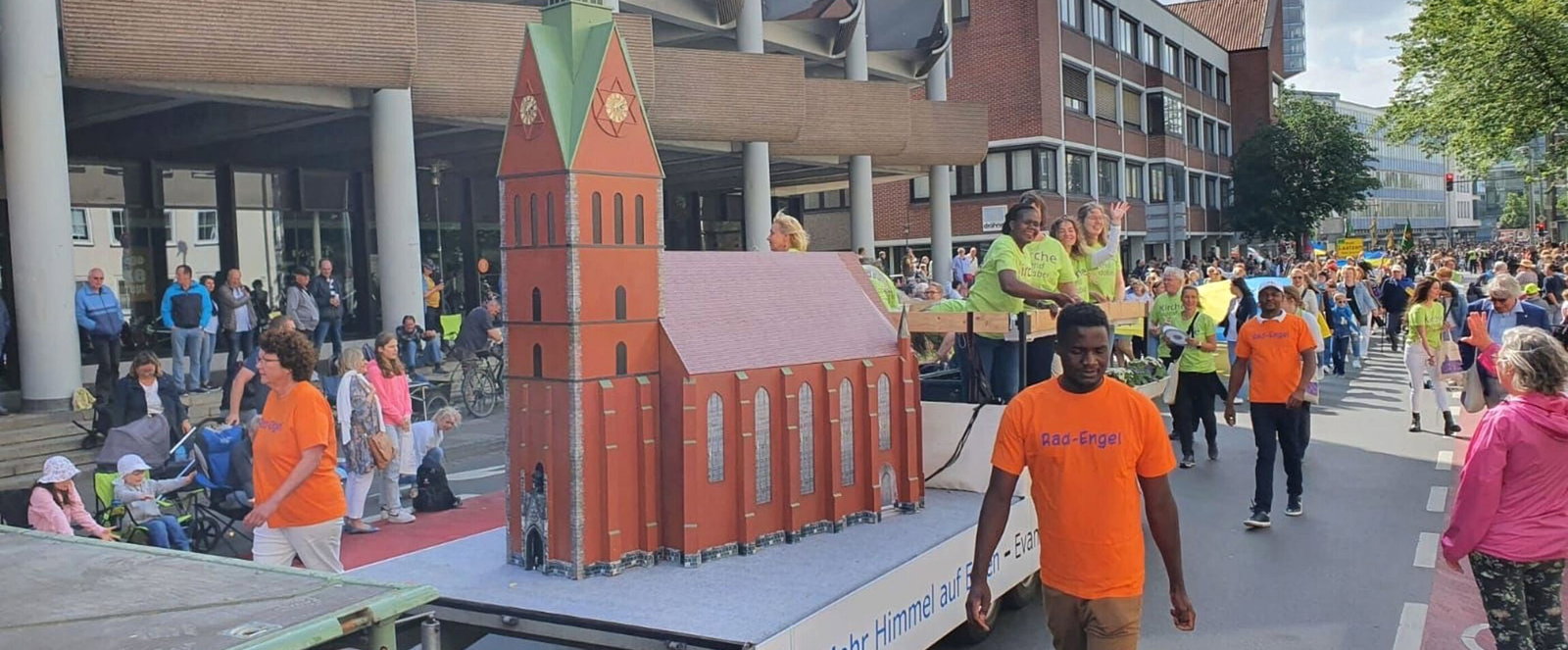 Mehrere Menschen ziehen mit einem Kirchenmodell auf einem Anhänger durch die Straße.