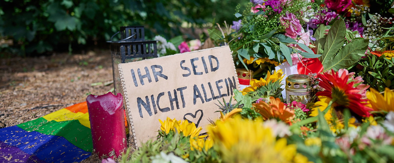Blumen und Beileidsbekundungen, darunter ein Schild mit der Aufschrift: Ihr seid nicht allein.
