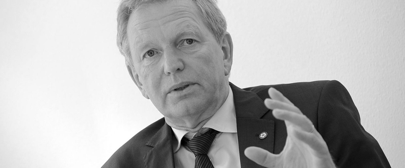 Schwarz-weiß-Bild einer als Mann lesbaren Person, die mit erhobener Hand spricht.