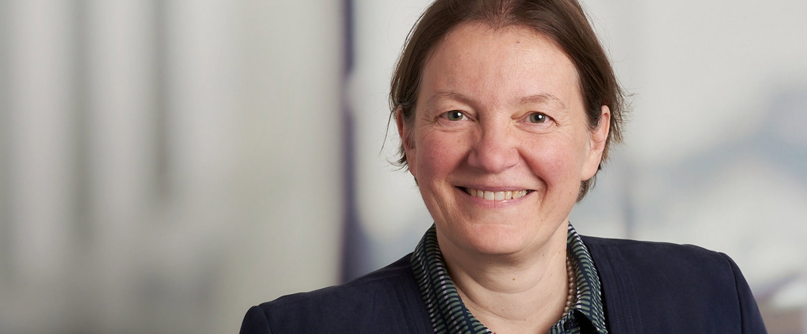 Portraitfoto einer als Frau lesbaren Person mit braunen zurückgebundenen Haaren.