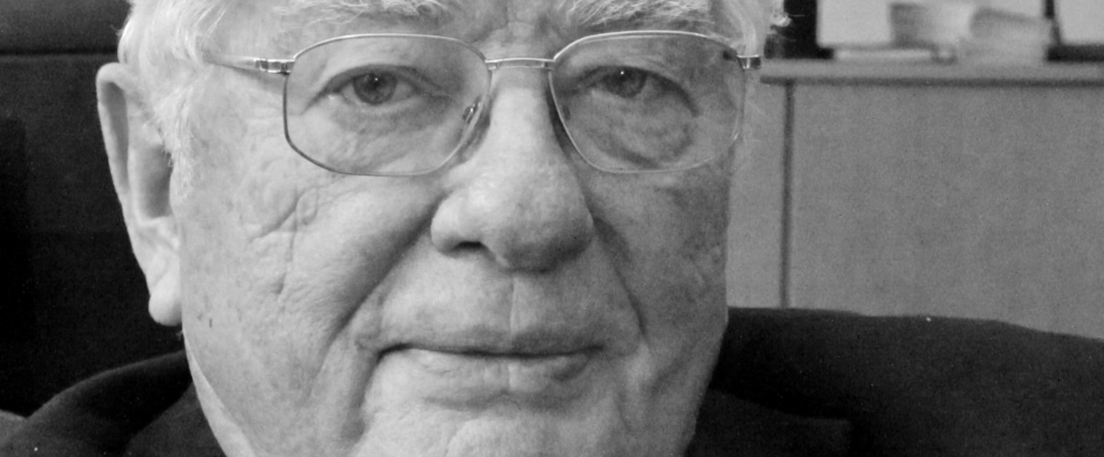 Eine männlich gelesene Person mit kurzen weißen Haaren und Brille. Das Bild ist in schwarzweiß.
