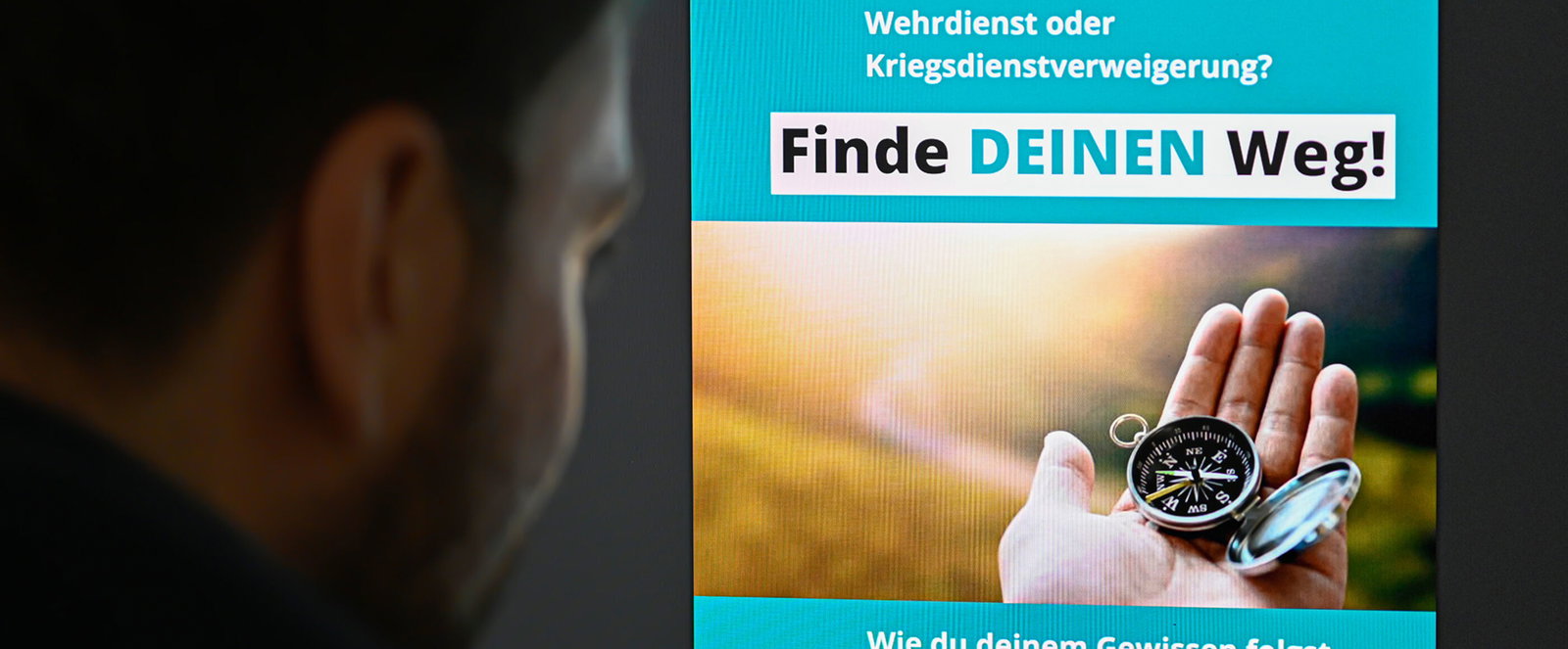 Eine als Mann lesbare Person schaut auf einen Bildschirm, auf dem die Titelseite der Broschüre „Finde deinen Weg“ zu sehen ist.