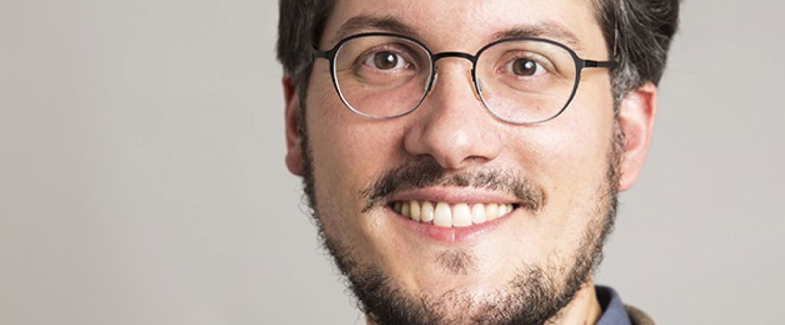 Eine jüngere als Mann lesbare Person mit Brille und braunen Haaren.