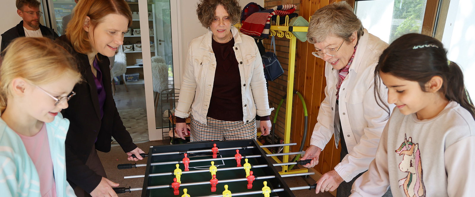 Drei erwachsene als Frauen und zwei als Mädchen lesbare Personen spielen Kicker 