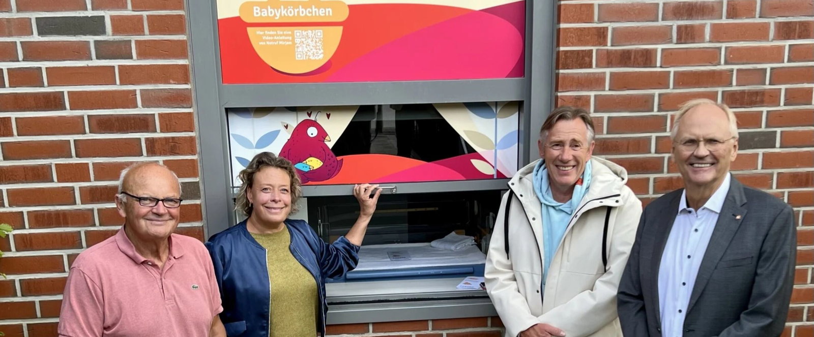 Vier Menschen stehen vor einem „Babykörbchen“ für Mütter in Not