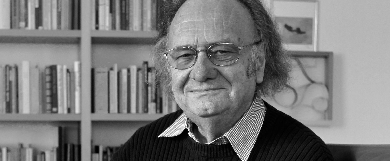 Eine männlich gelesene Person mit Brille und längerem grauen Haar. 