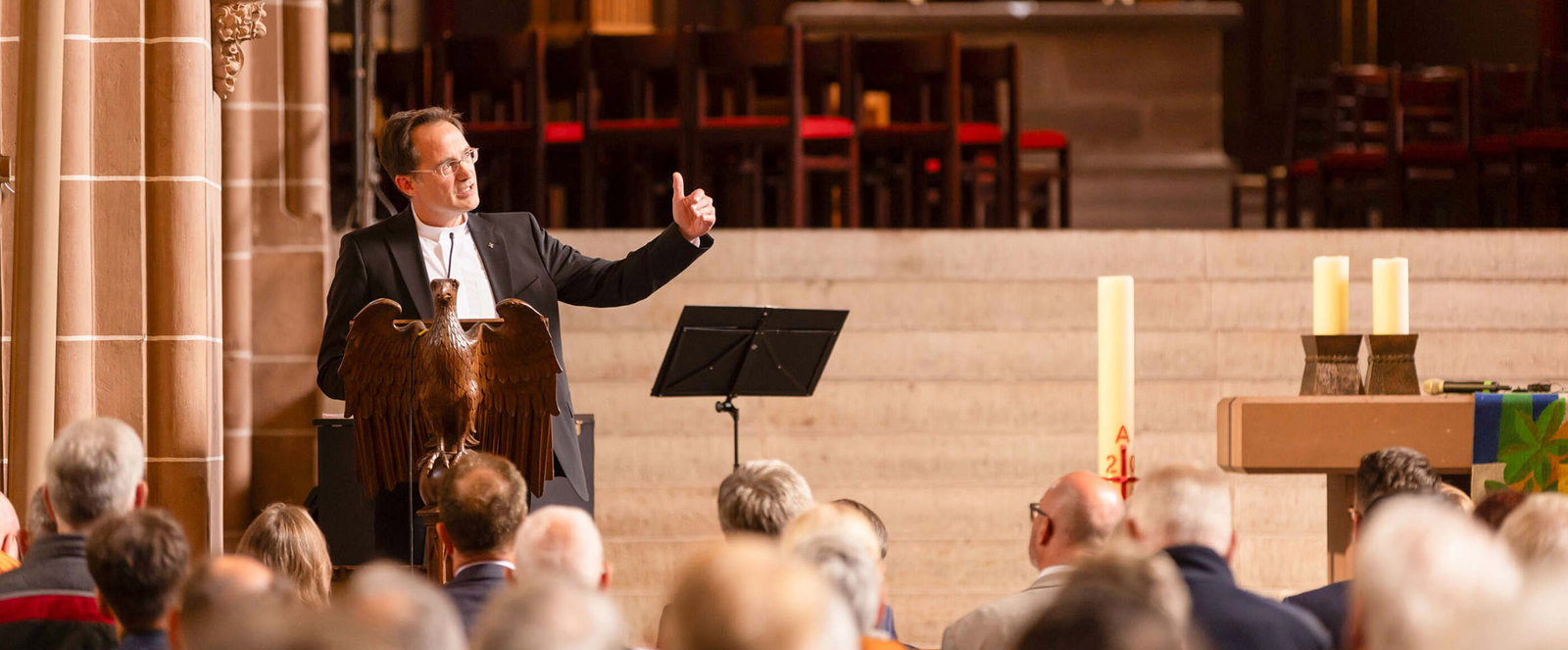 Eine als Mann lesbare Person im Anzug spricht vor Publikum in einer Kirche