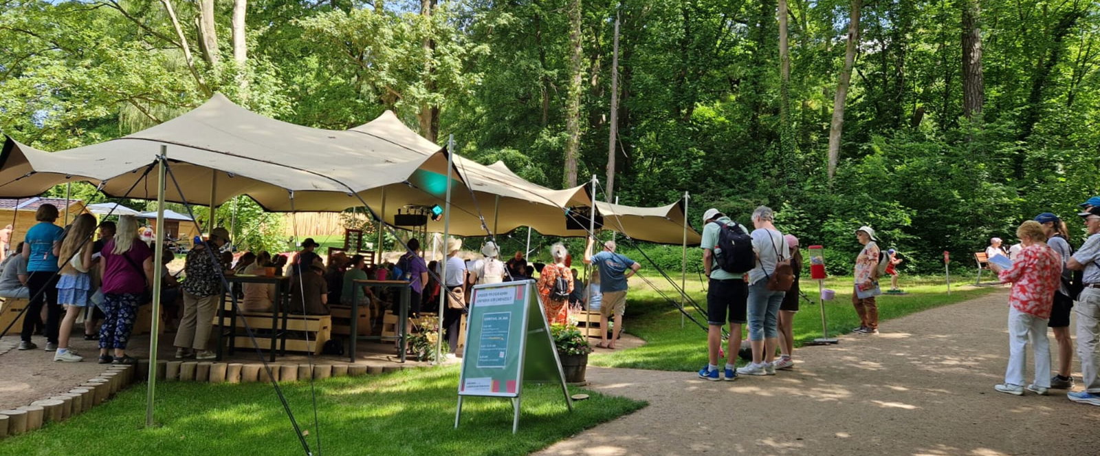 Ein großes Zeltdach im Grünen, besucht von mehreren Menschen
